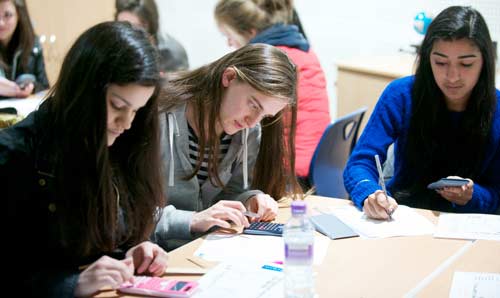 Three female students sat at a table writing and typing on calculators